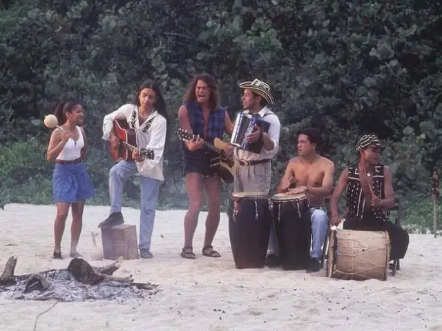 A group of musicians playing on the beach with guitars, accordion and drums.